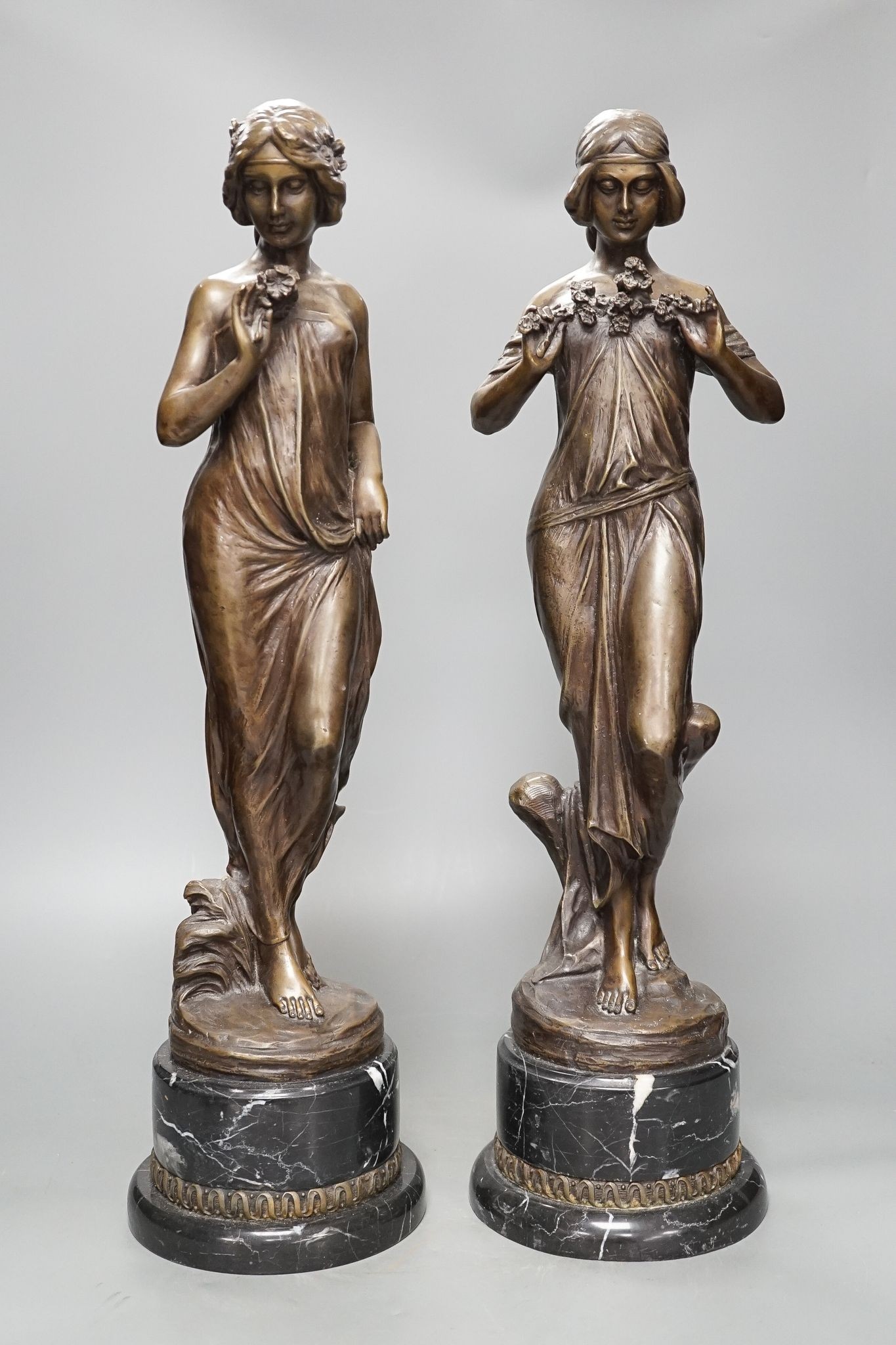 After Jean-Antoine Houdon, (French 1741-1828), a pair of bronze figures of lady’s holding flowers, on marble bases, 52cm